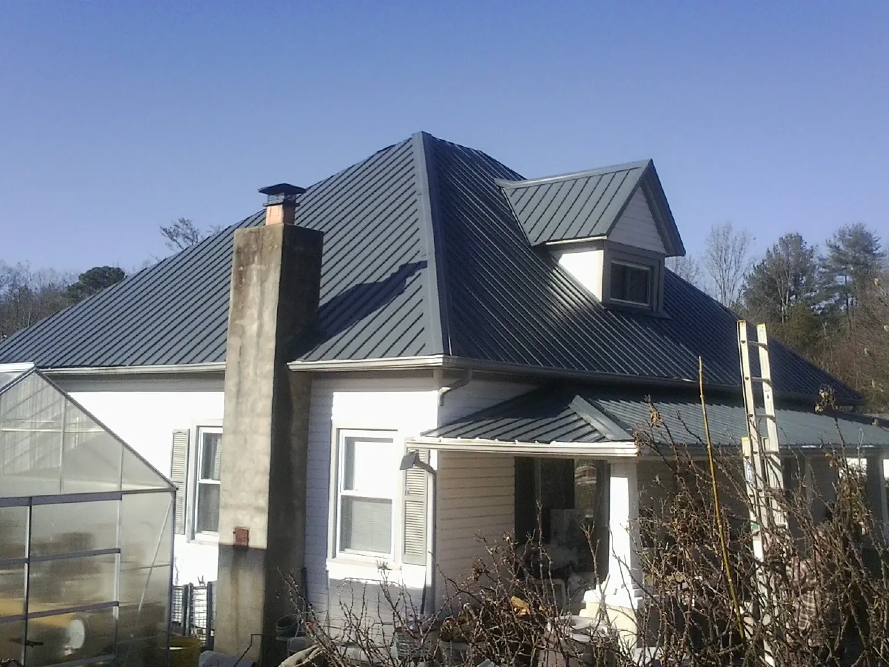 Dark blue standing seam metal roof on a white farmhouse with dormer — Slate & Tile Roof Repair by Roofing Brothers in West Creek