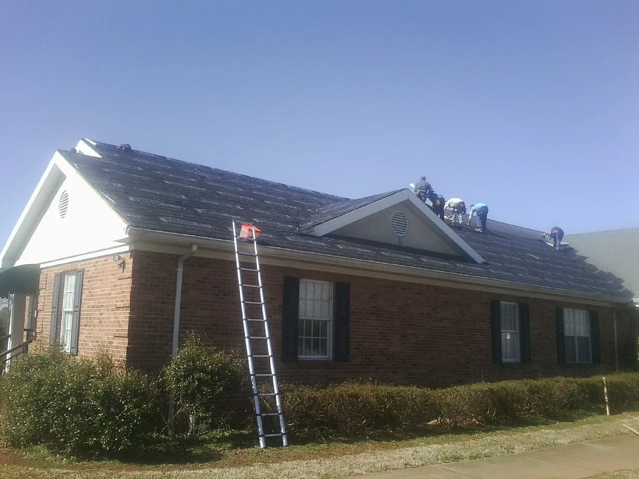 Crew tearing shingles off a brick ranch roof with a ladder set — Metal Roof Repair work by our crew in West Creek