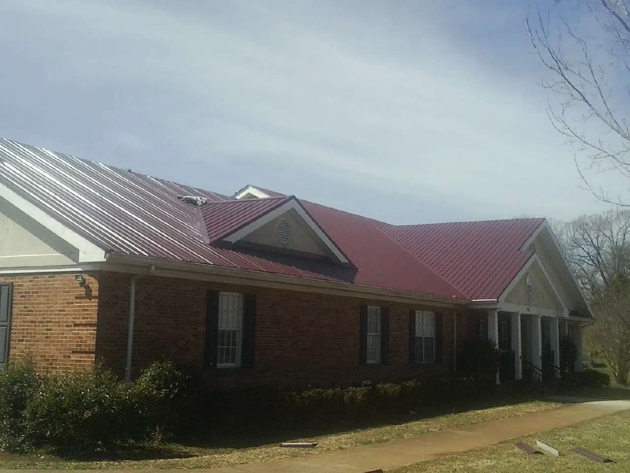 Red metal roof with gabled entries on a long brick building, from a Hail Damage Roof Repair job in West Creek