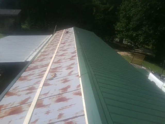 Old rusted panels beside newly installed green metal roofing — Wind Damage Roof Repair by Roofing Brothers in West Creek