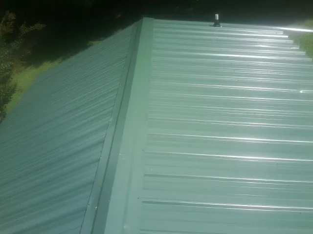 New green metal panels meeting at the ridge of a roof — Flat Roof Repair work by our crew in West Creek