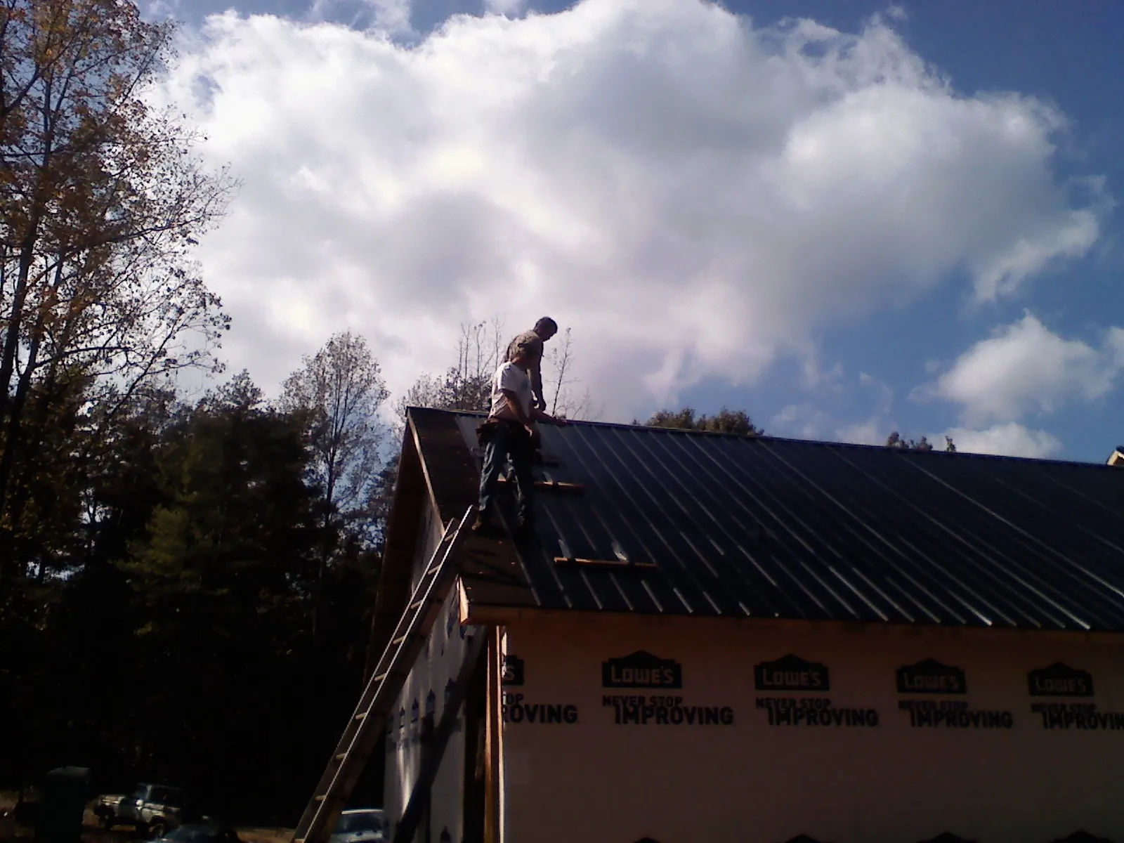 Roofer fastening dark metal panels high against a cloudy sky, from a Roof Inspection job in West Creek