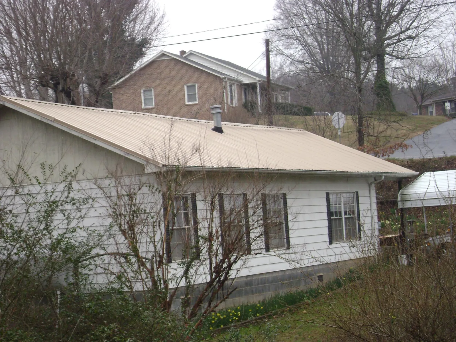 Tan metal roof on a white sided house set into a hillside — Commercial Roofing by Roofing Brothers in West Creek