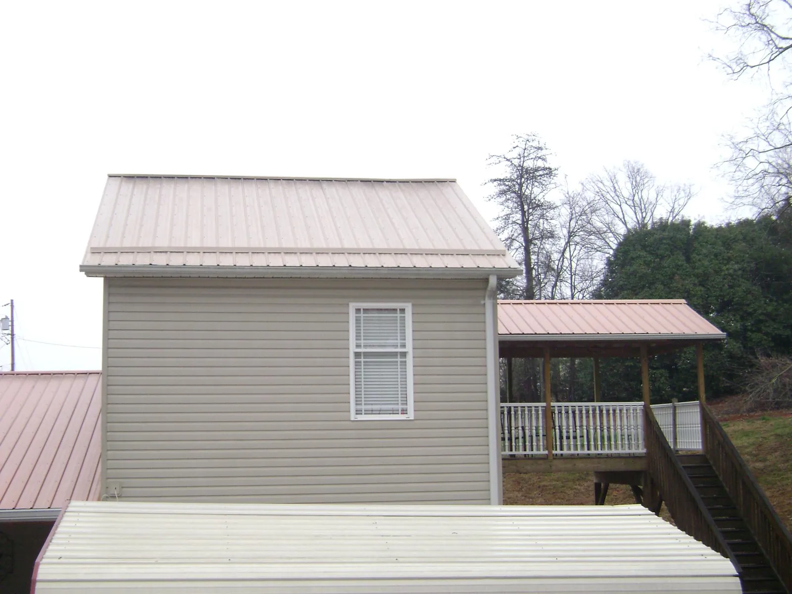 Tan metal roofs on a two story addition and attached porch, from a Roof Replacement job in West Creek
